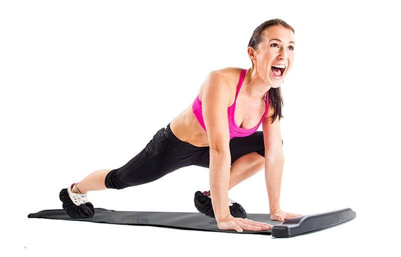 A woman in a pink sports bra and black leggings performs a lunge exercise on a black yoga mat against a solid white background.