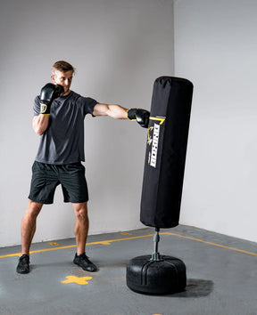 Person wearing boxing gloves and shorts, training with a punching bag in a room.